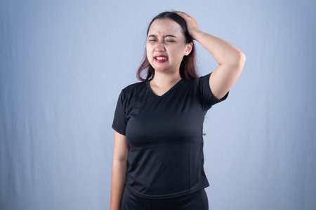 A woman in a black shirt winces with a hand on her headの写真素材