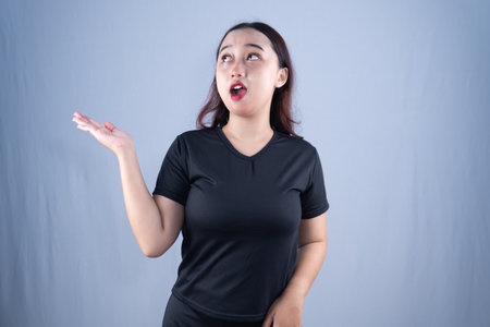 A surprised woman in a black shirt looks up and holds her hand outの写真素材