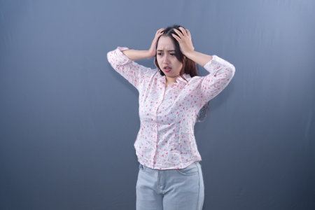 A woman in a floral shirt and jeans holds her head.の写真素材