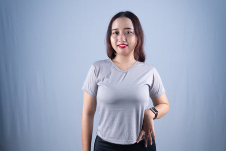 A smiling woman in a gray t-shirt and black bottoms stands against a light backgroundの写真素材