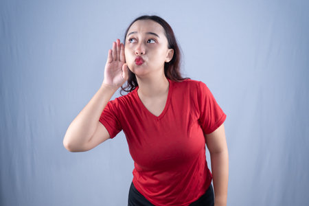 A woman in a red shirt is listening intently, with her hand cupped to her earの写真素材