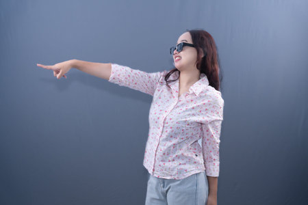 A woman in a white and pink floral shirt and sunglasses is pointing left while laughing