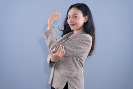 A smiling woman in a beige blazer flexes her bicep, showing strengthの写真素材