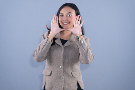 A woman in a beige blazer is framing her face with her hands and smilingの写真素材