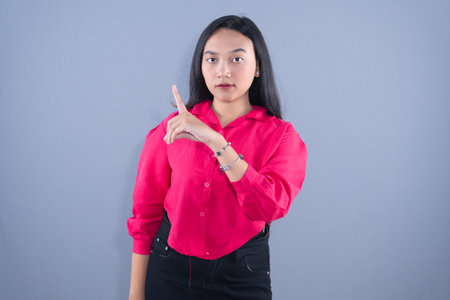 A young woman in a pink shirt is pointing her finger up against a gray backgroundの写真素材