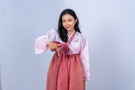 Young Asian woman in traditional Korean pink Hanbok dress points down on a light backgroundの写真素材