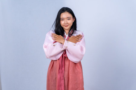 A smiling young woman in a pink hanbok crosses her arms over her chest against a light background
