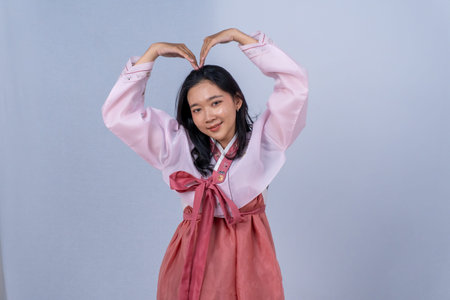 Smiling young woman in pink hanbok making a large hand heart gestureの写真素材