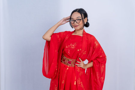 A young woman in a red and gold traditional outfit and glasses poses confidentlyの写真素材