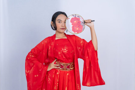 A young woman in a traditional Chinese outfit poses with a red floral fanの写真素材