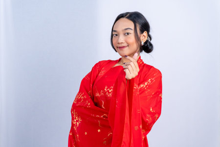 A woman in a red Chinese Hanfu makes a finger heart with a smile against a white studio backgroundの写真素材