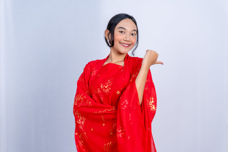 A woman in a red Chinese dress winks with both hands raised against a simple white studio backgroundの写真素材