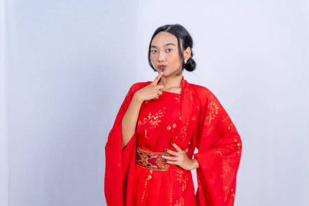 A woman in a red Chinese dress puts a finger to her lips with a smile against a white backgroundの写真素材