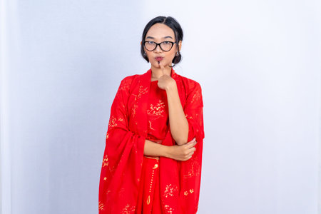 A young woman in a traditional Chinese outfit and glasses poses, finger to chinの写真素材