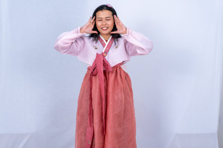 A woman in pink and red Korean Hanbok shouts with hands near her face against a white backgroundの写真素材