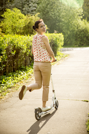 Beautiful young woman on push scooter in a parkの写真素材
