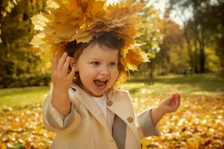 Happy cute baby girl with garland from yellow leaves on her headの写真素材
