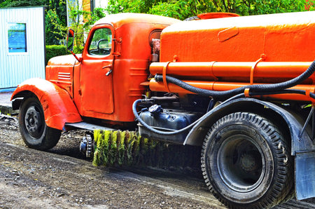 An old retro water truck based on a truck. Fragments of an orange car.