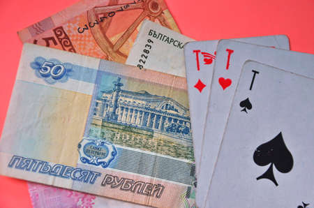 Playing cards and money from different countries on a pink background.の写真素材