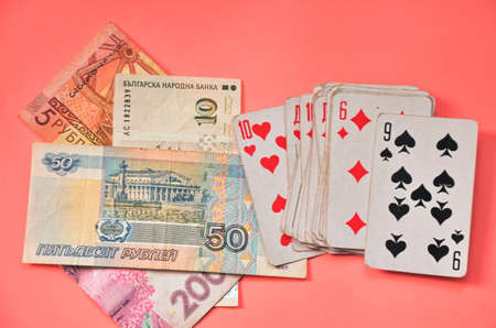 Playing cards and money from different countries on a pink background.の写真素材