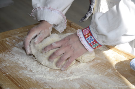 A woman in a national suit will mix the dough with her hands. Baking traditional birds (skylark) from the dough in spring. Ukrainian national tradition. Selective focus of the image.の写真素材