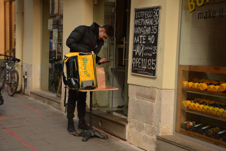 Lviv, Ukraine - January 2021: A deliveryman for Glovo in center of Lviv. Ukraine shutdowns bars, restaurants and shopping malls to stem the spread of the coronavirus.のeditorial素材