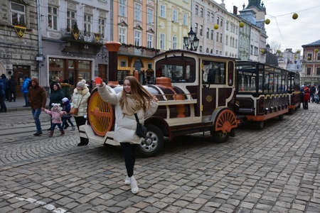 Lviv, Ukraine. 7 January 2021. Tourist tram on the main square of Lviv. Ancient buildings, pavers and crowds of tourists in the Rynok Square.Excursions on Christmas days.のeditorial素材
