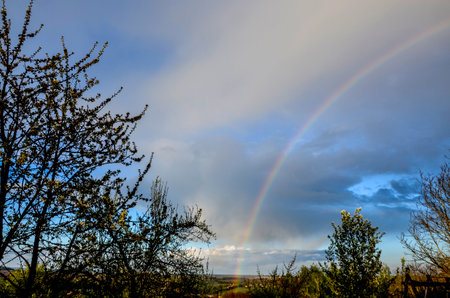 a beautiful, colorful rainbow against the background of a dangerous, stormy sky over a rural farmの写真素材