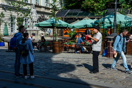 Lviv, Ukraine, July 2021. Crowded city. Tourist entertainment - street photographer shoots on retro camera.のeditorial素材
