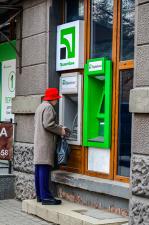 Lviv.Ukraine.November 2022.Facade of the state bank of Ukraine "Privatbank" in the city of Lviv.Nationalized by the government of Ukraine .A woman wearing a red hat outside an ATM.のeditorial素材