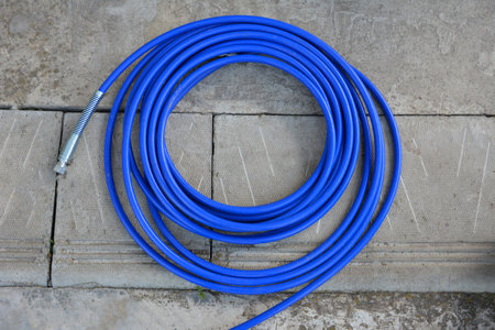 The blue hose of the spray gun is lying on the concrete.A long blue hose is wrapped in a ring.Special equipment for painting and whitewashing.の写真素材