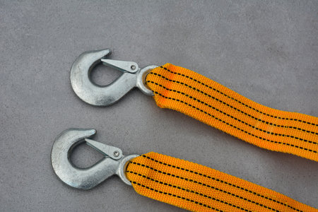 Towing strap with steel hooks, on a gray background, top view. Vehicle safety.tow strap rope of yellow or orange color with hooksの写真素材