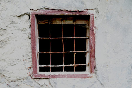 Old window with metal bars set in a stone wall of an abandoned building. Cracked plaster, rough...