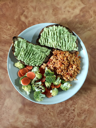 Healthy meal with avocado toast, broccoli and carrot side dish and scramble on a plate. Top view,...