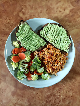 Healthy meal with avocado toast, broccoli and carrot side dish and scramble on a plate. Top view,...