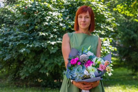 Portrait of a beautiful happy red-haired girl who holds a spectacular stylish bouquet of different flowers. Gift from a man for his birthday. The concept of the 8th of March, the International Women's Dayの写真素材