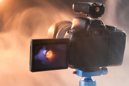 Photo of the camera on a blue tripod that photographs in the studio a professional lighting device in the smoke. Studio lights and smoke equipment. Camera with radio synchronizerの写真素材