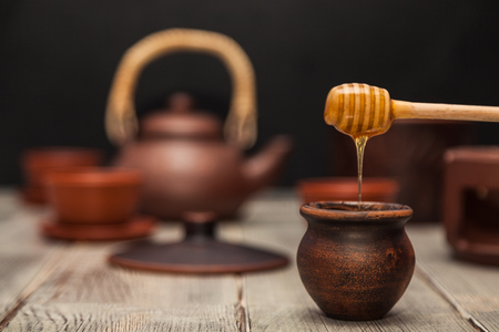 Tea ceremony, tea party. Clay dishes. Honey flows from a wooden spoon into a pot. Still lifeの写真素材
