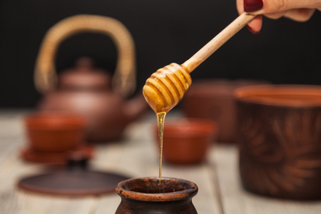 Tea ceremony, tea party. Clay dishes. Honey flows from a wooden spoon into a pot. Still lifeの写真素材