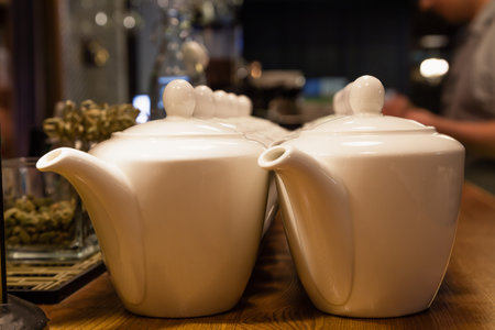 Many white ceramic teapots with round lids stand on the wooden bar counter in the restaurant. Concept dishes in cafe, tea, breakfastの写真素材