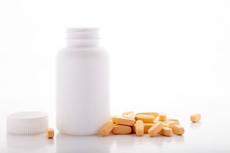 Closeup scattered from white pill bottle orange oval medicine vitamins for pregnancy, pills, drugs isolated on white background. Healthy food dietary supplementの写真素材