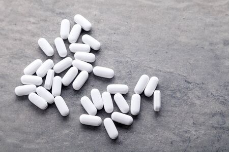 Closeup scattered white medicine vitamins, pills, drugs on gray background. White food dietary supplement. Black and white photography. Top viewの写真素材