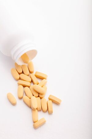 Closeup scattered from white pill bottle orange oval medicine vitamins for pregnancy, pills, drugs isolated on white background. Healthy food dietary supplement. Verticalの写真素材