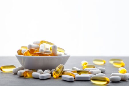 Assortment scattered pharmaceutical medicine vitamins, pills, drugs in bowl on gray background. White food dietary supplement hard shelled capsules filled with powder, salmon oil softgel Omega 3の写真素材