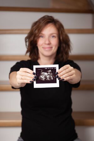 Pregnant woman feeling happy at home while taking care of her child. The young expecting mother holding baby in pregnant belly. Maternity prenatal care and a woman pregnancy conceptの写真素材