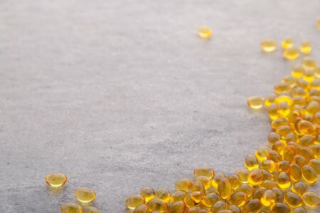 Top view of scattered Gold fish oil in bowl isolated for good health on gray background. Food dietary supplement, salmon fish oil softgel Omega 3, pharmaceutical medicine vitamin D capsulesの写真素材