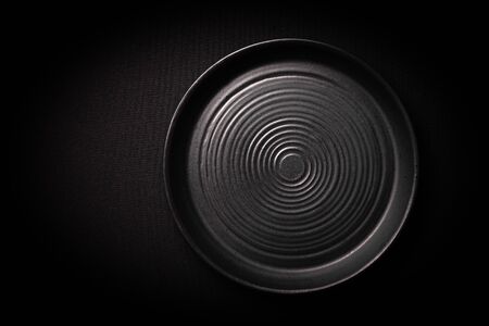 Closeup empty round black ceramic plate with pattern of circles on dark background with copy space. Concept modern shooting menu from chef, restaurant advert, tableware catalogs, top viewの写真素材