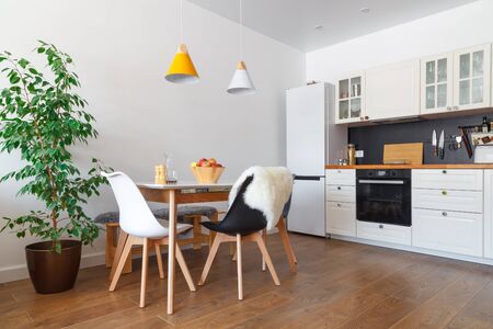 Modern interior of cozy kitchen, dining room, white furniture, wall, black accessories, natural materials, wooden chairs, green flower in pot. Concept scandinavian design apartment of young familyの写真素材