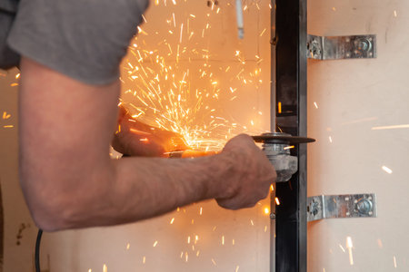Worker cuts black metal installation with anelectric angle grinder, sparks fly around