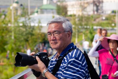 Russia Moscow 2019-06-17 Hobby and travel. Old man in taking photo with his camera in park, summer, outdoors. Traveling Asian male tourist backpackers taking photo.のeditorial素材